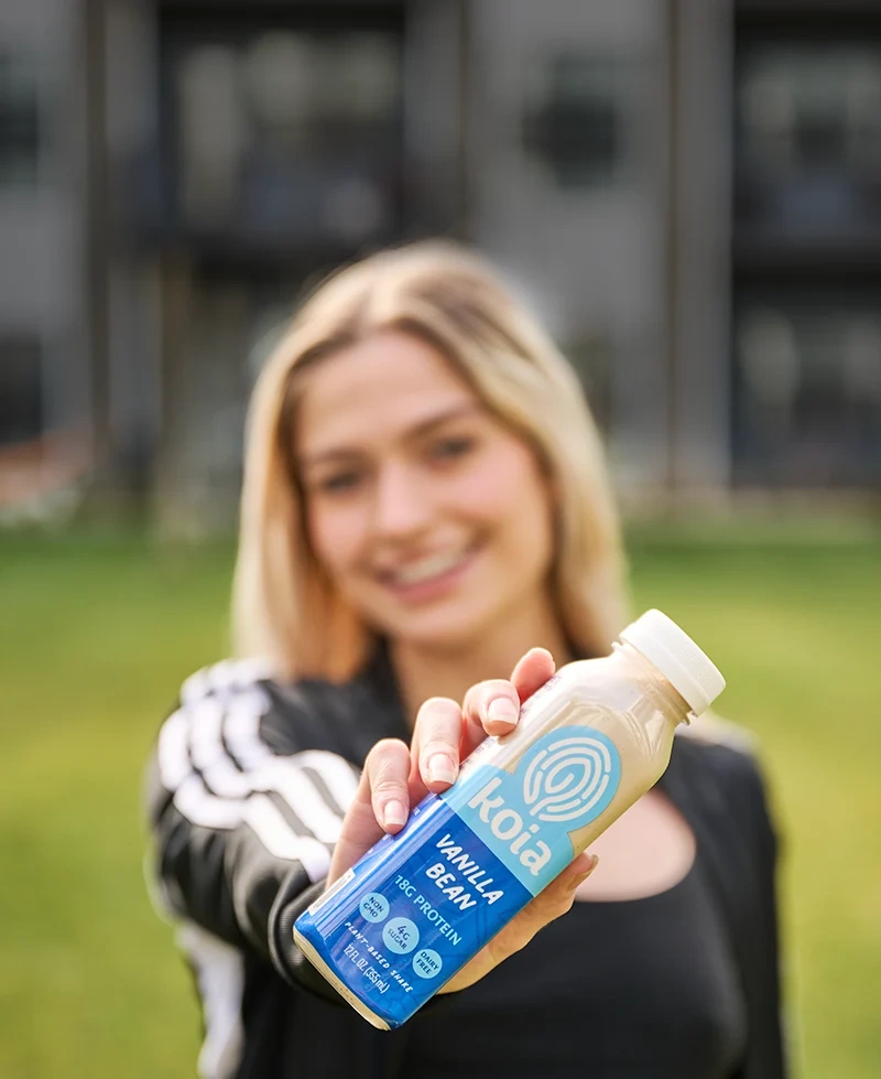 A woman holding a Koia bottle